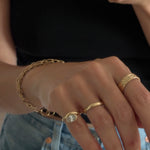 mirror selfie focused on the hand wearing a custom gold link chain, custom wave textured gold ring, a half round gold band, and a pinky ring with an organic curved ring around a bezel 1ct diamond. 
