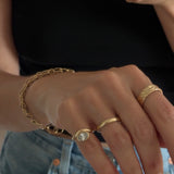mirror selfie focused on the hand wearing a custom gold link chain, custom wave textured gold ring, a half round gold band, and a pinky ring with an organic curved ring around a bezel 1ct diamond. 